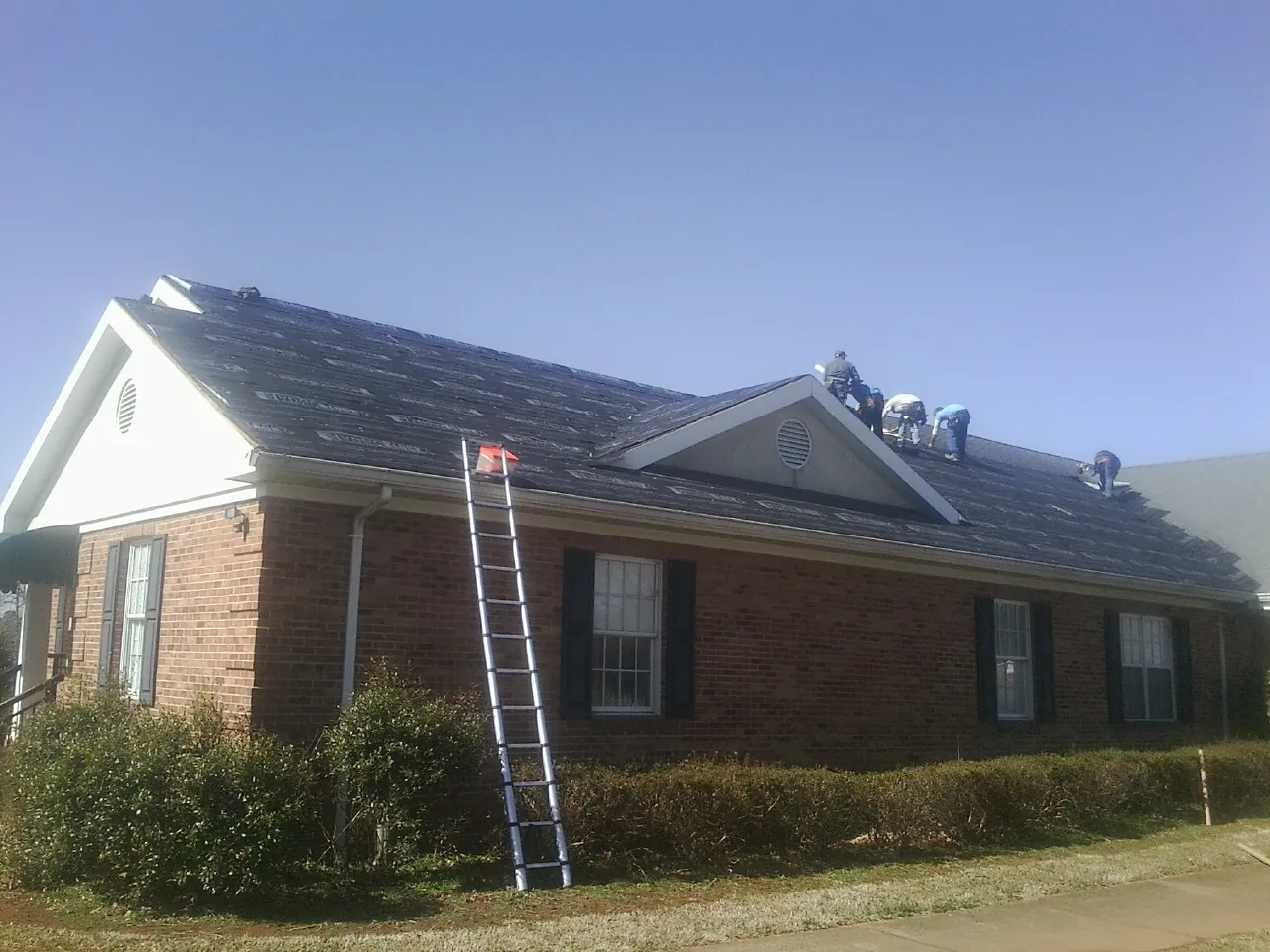 Crew tearing shingles off a brick ranch roof with a ladder set — Emergency Roof Repair work by our crew in Green Lane