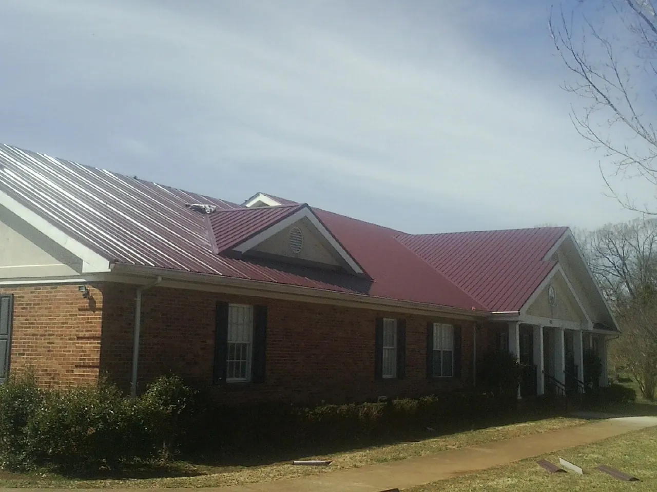 Red metal roof with gabled entries on a long brick building, from a Hail Damage Roof Repair job in Green Lane