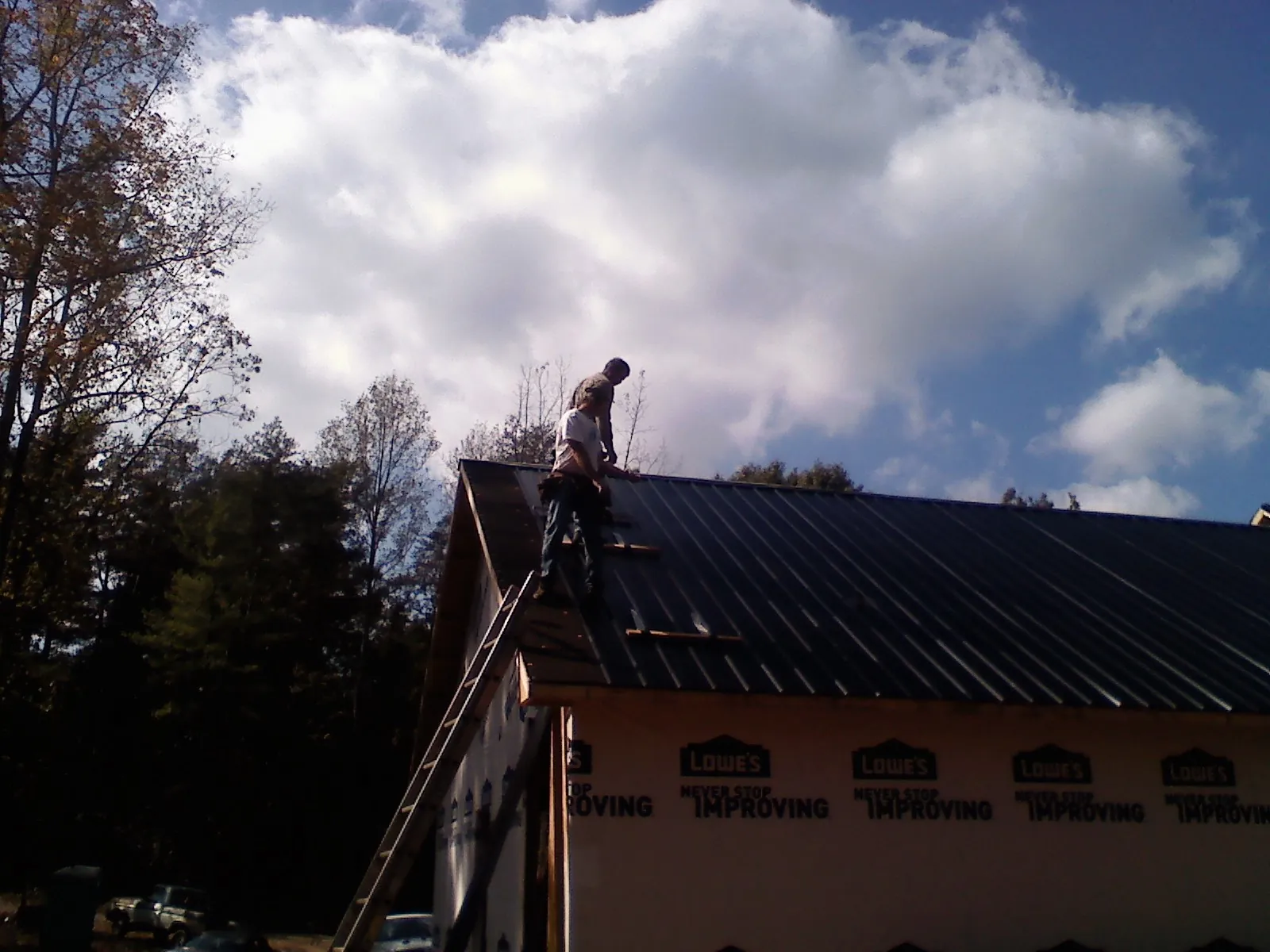 Roofer fastening dark metal panels high against a cloudy sky, from a Roof Inspection job in Green Lane