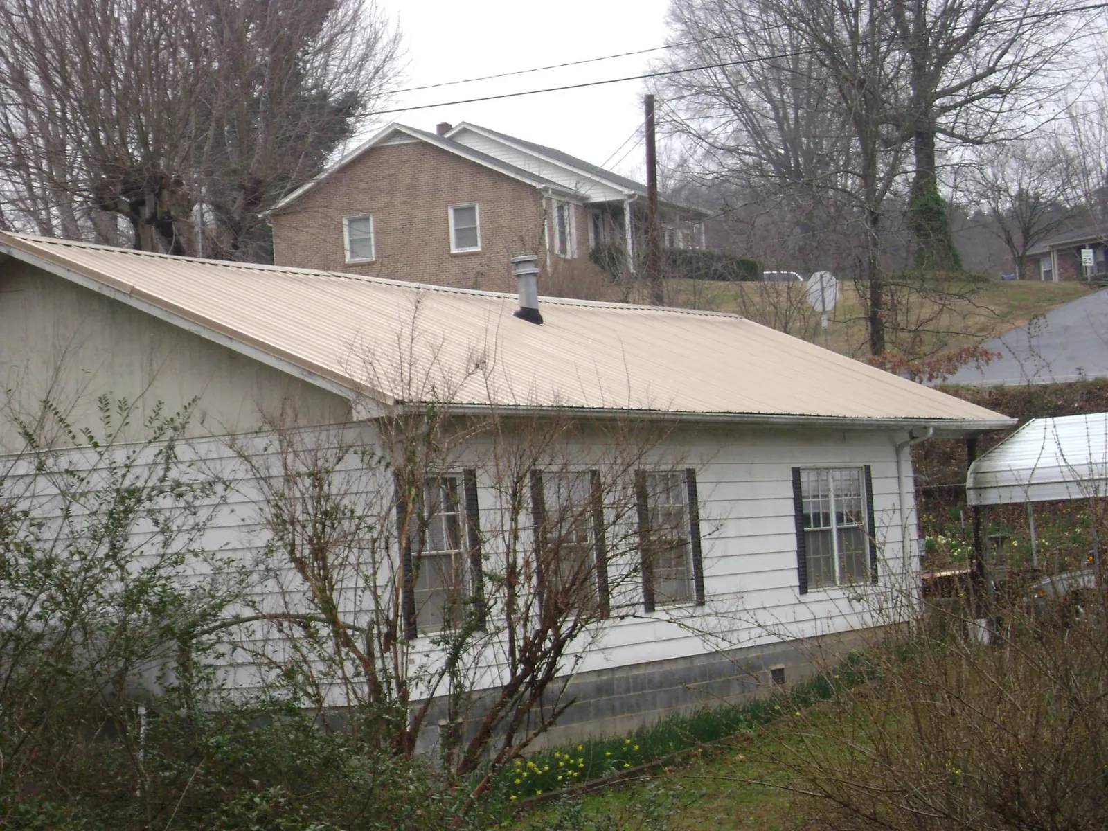 Tan metal roof on a white sided house set into a hillside — Commercial Roofing by Roofing Brothers in Green Lane