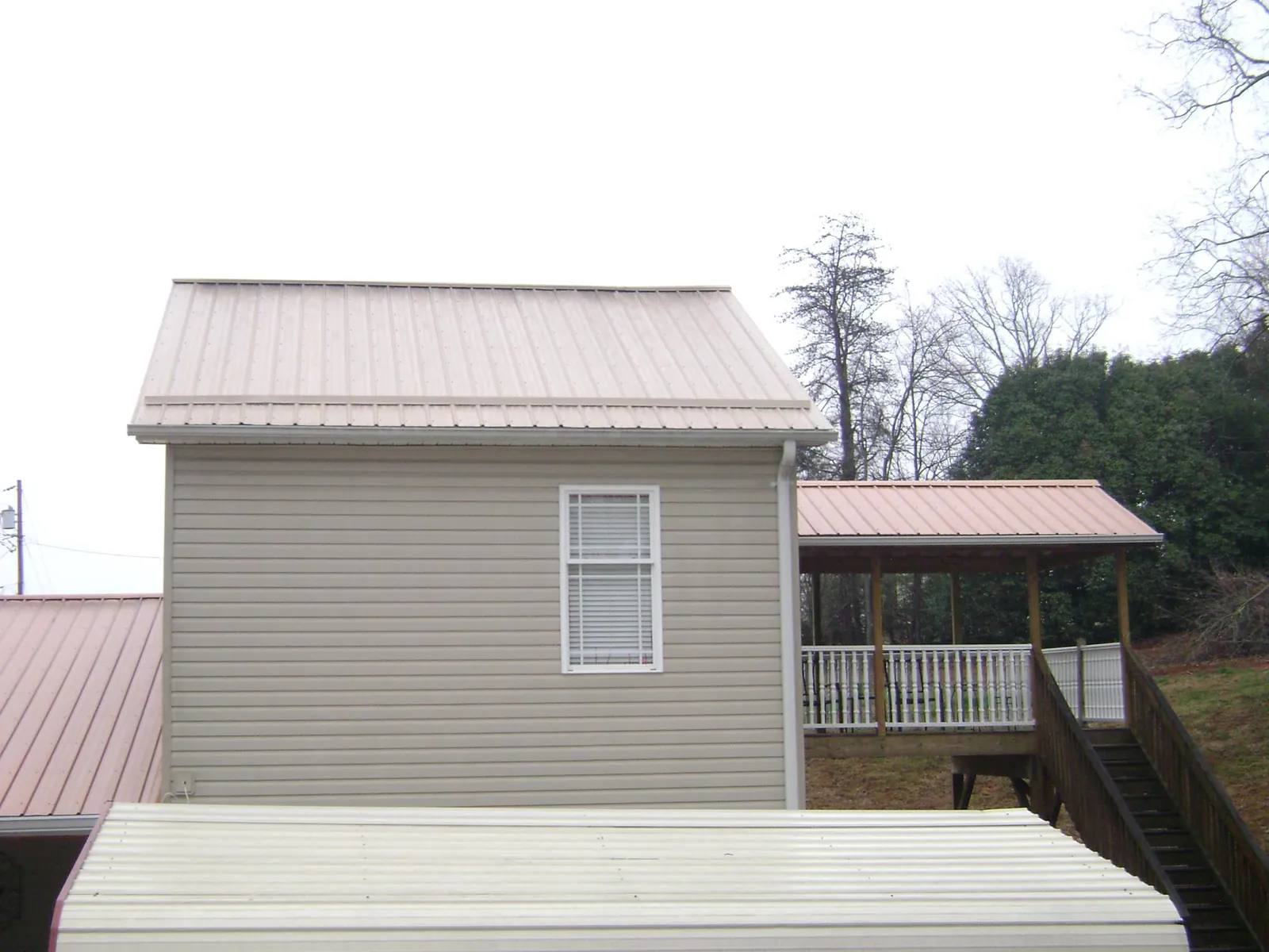 Tan metal roofs on a two story addition and attached porch, from a Roof Replacement job in Green Lane